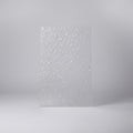 A textured clear polycarbonate sheet with a dense, reflective mosaic pattern, standing upright on a desk with an office background.