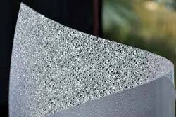 A close-up of a textured silver glitter fabric or material draped over a white surface, showing a sparkling, reflective pattern.